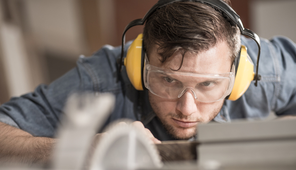 Arbeit - Porträt eines Mannes mit Ohrenschützer und Schutzbrille vor einer Werkbank